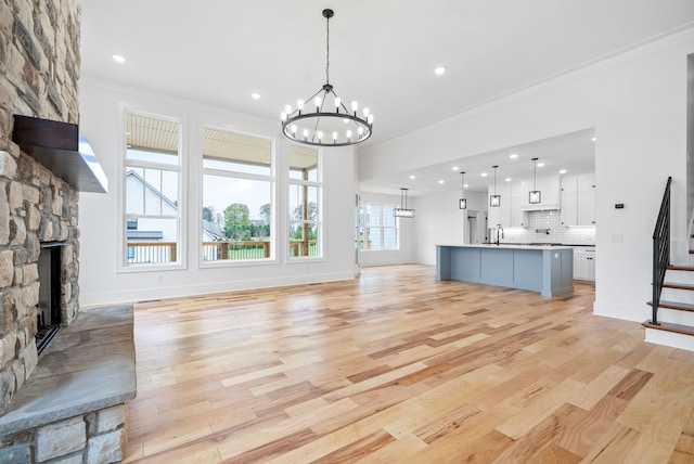 unfurnished living room with crown molding, a stone fireplace, a notable chandelier, sink, and light hardwood / wood-style flooring