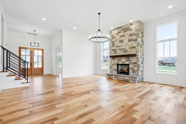 unfurnished living room featuring a stone fireplace, light wood-type flooring, a chandelier, and ornamental molding