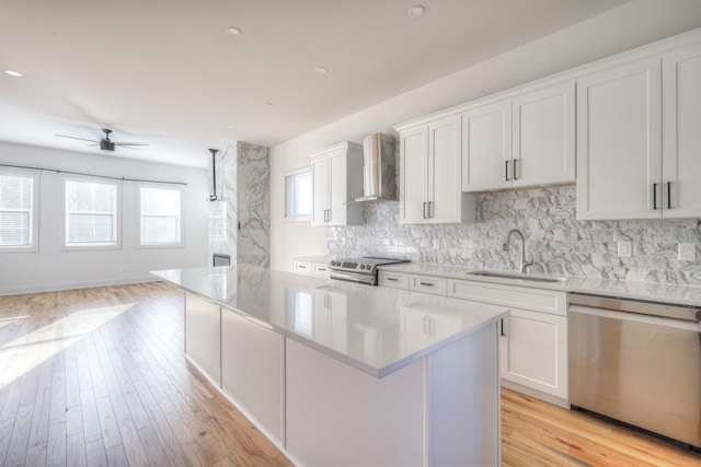 kitchen with light hardwood / wood-style flooring, appliances with stainless steel finishes, wall chimney exhaust hood, and white cabinets