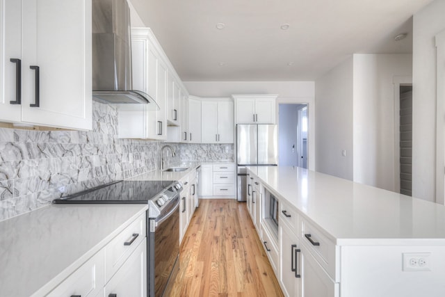 kitchen with stainless steel appliances, white cabinetry, wall chimney exhaust hood, a center island, and light wood-type flooring