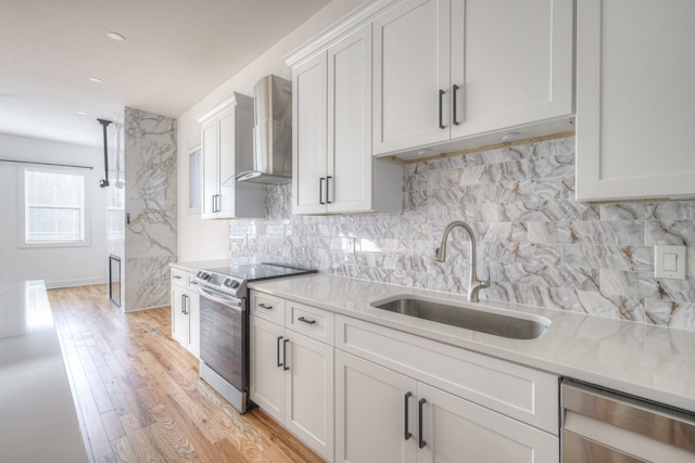 kitchen featuring stainless steel appliances, sink, white cabinets, wall chimney range hood, and light wood-type flooring