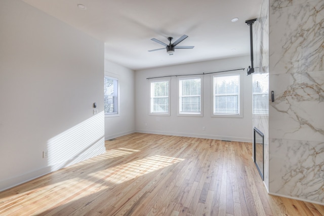 spare room featuring light wood-type flooring, tile walls, a high end fireplace, and ceiling fan