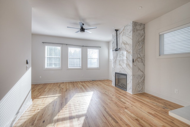 unfurnished living room with a high end fireplace, ceiling fan, and light hardwood / wood-style flooring