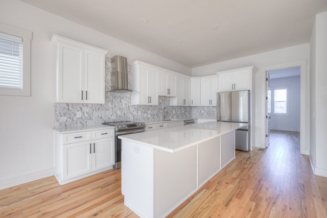 kitchen featuring white cabinetry, appliances with stainless steel finishes, light hardwood / wood-style flooring, a kitchen island, and wall chimney range hood