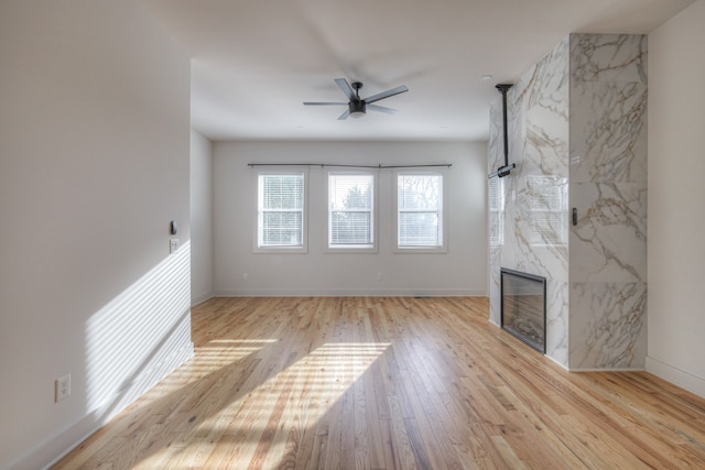 unfurnished living room with light wood-type flooring, ceiling fan, and a high end fireplace