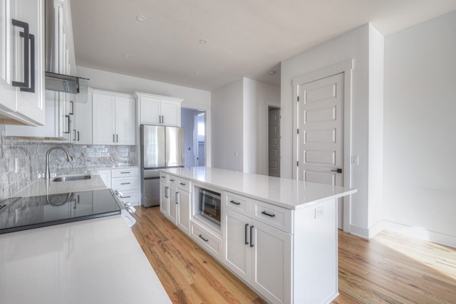 kitchen with light hardwood / wood-style floors, stainless steel appliances, sink, a kitchen island, and white cabinetry