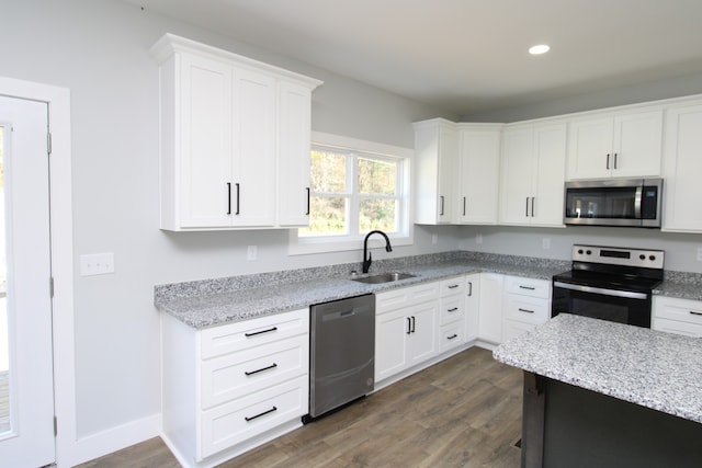 kitchen with light stone counters, appliances with stainless steel finishes, sink, white cabinets, and dark wood-type flooring