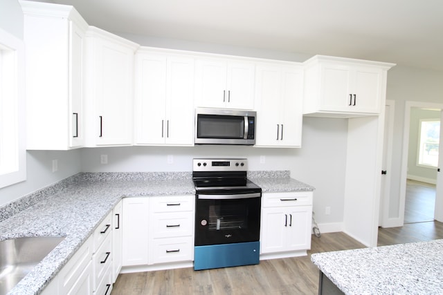 kitchen with light stone counters, appliances with stainless steel finishes, sink, white cabinets, and light hardwood / wood-style flooring