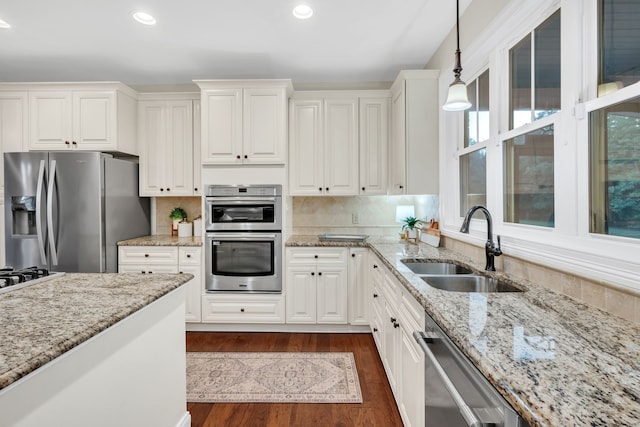 kitchen with stainless steel appliances, white cabinetry, sink, and decorative light fixtures