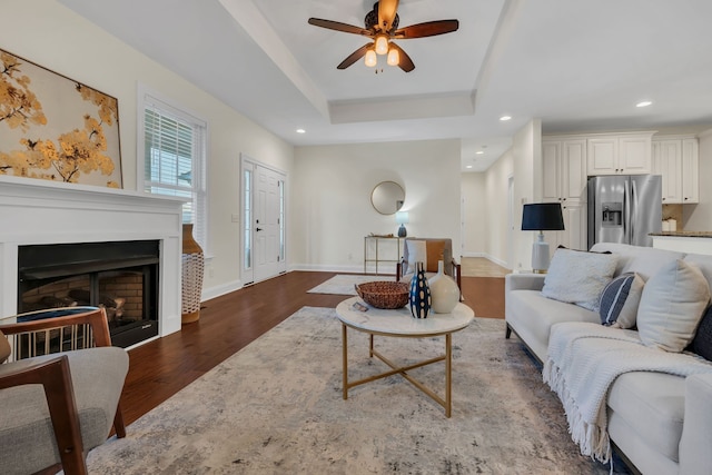 living room featuring dark hardwood / wood-style floors, a raised ceiling, and ceiling fan