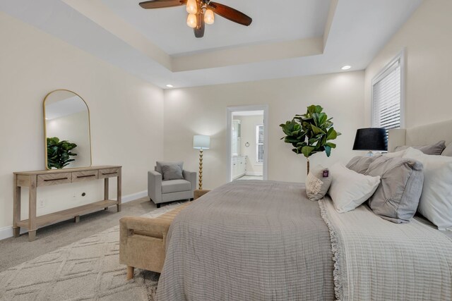 bedroom featuring ensuite bath, a raised ceiling, light carpet, and ceiling fan