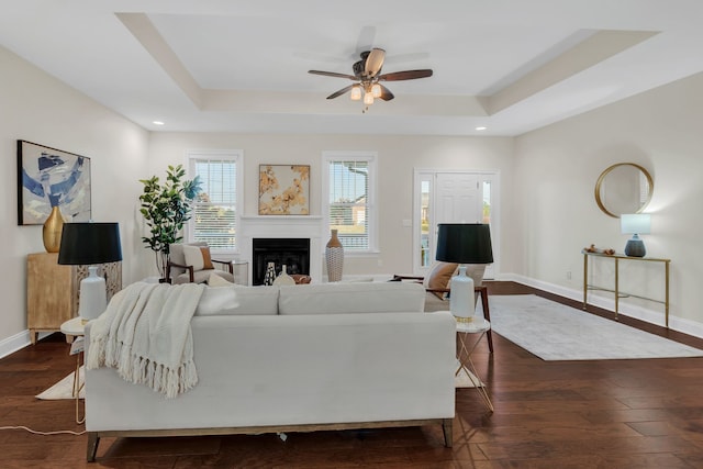 living room featuring dark wood-type flooring, ceiling fan, and a tray ceiling