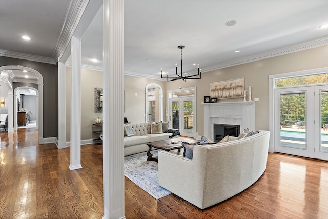 living room featuring hardwood / wood-style flooring, ornate columns, crown molding, and a notable chandelier