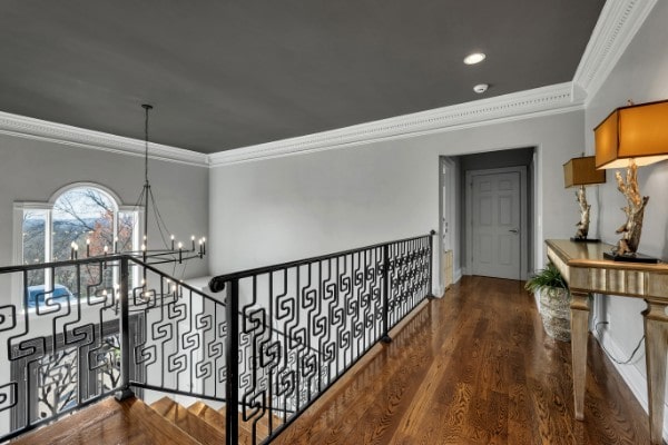 hallway featuring wood-type flooring, crown molding, and a notable chandelier