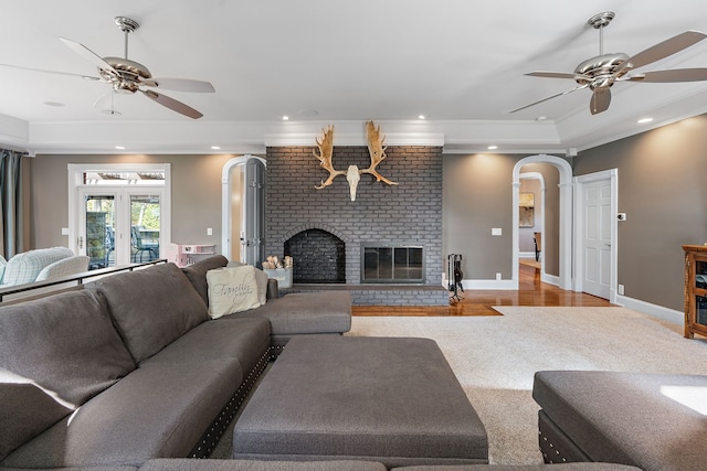 living room featuring light wood-type flooring, a raised ceiling, ceiling fan, and a brick fireplace