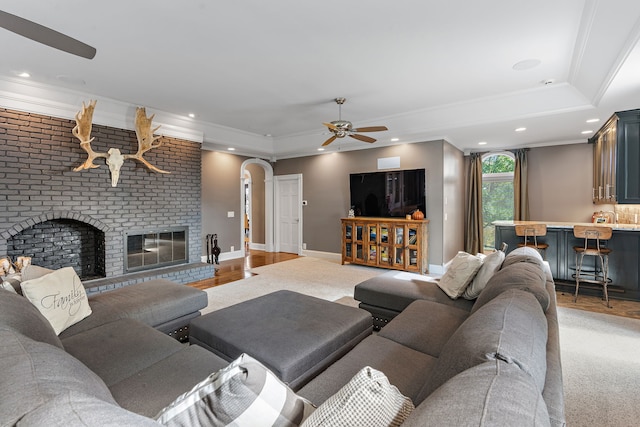 living room featuring ornamental molding, a fireplace, a raised ceiling, hardwood / wood-style flooring, and ceiling fan