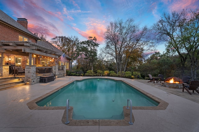 pool at dusk with a pergola, an outdoor fire pit, a patio area, and exterior kitchen