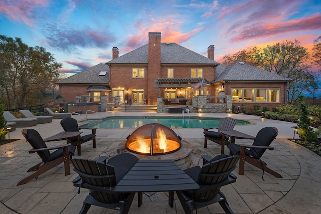 pool at dusk with a hot tub, an outdoor kitchen, a fire pit, and a patio area