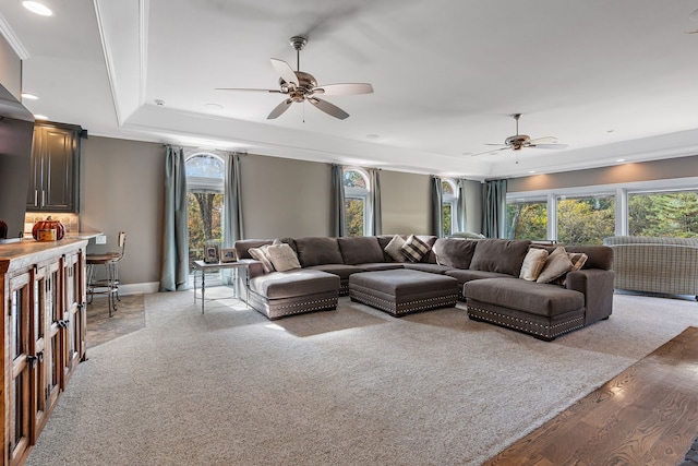 living room featuring light hardwood / wood-style floors, ceiling fan, a raised ceiling, and ornamental molding