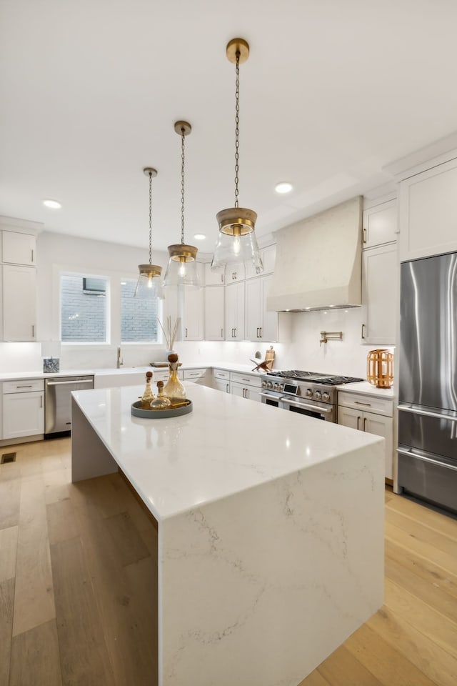 kitchen with premium range hood, a kitchen island, white cabinetry, light wood-style floors, and appliances with stainless steel finishes