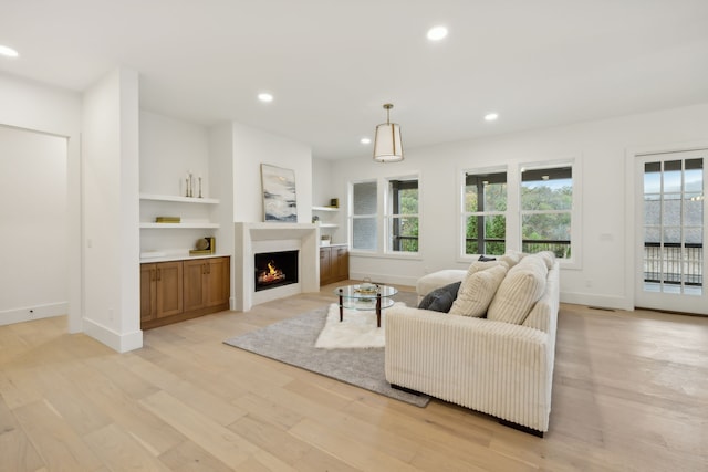 living area featuring recessed lighting, light wood-type flooring, baseboards, and a warm lit fireplace