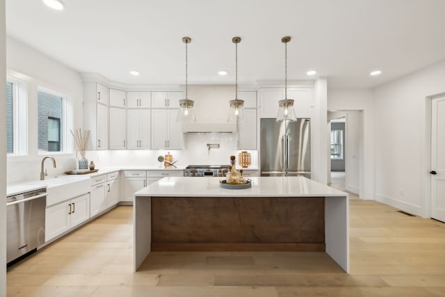 kitchen with light wood finished floors, a center island, premium range hood, appliances with stainless steel finishes, and white cabinets