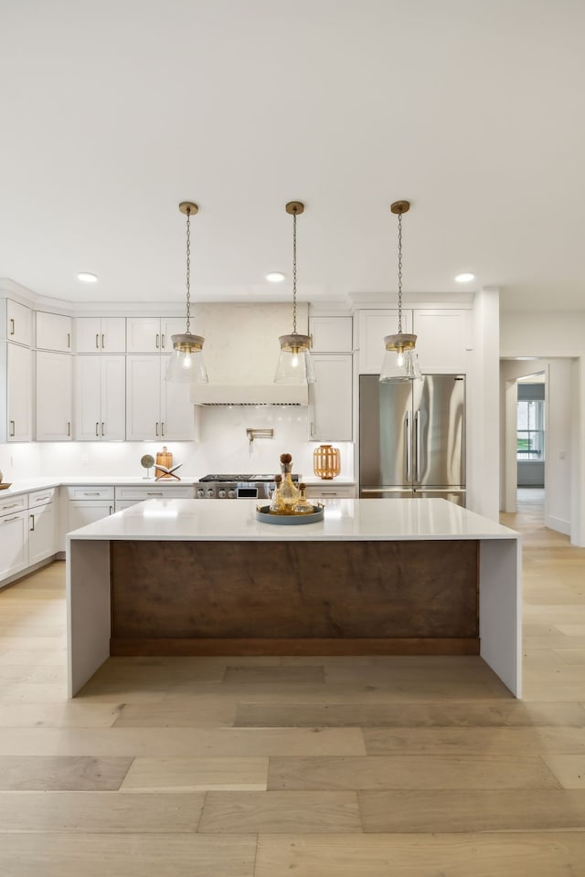 kitchen with light wood finished floors, a spacious island, light countertops, white cabinets, and high end refrigerator