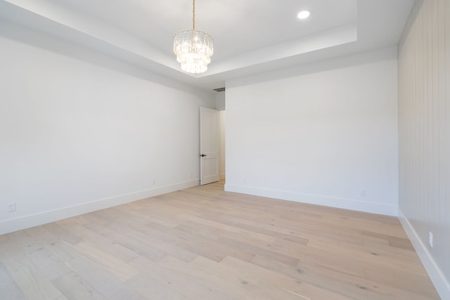 spare room featuring baseboards, a raised ceiling, and light wood-style floors