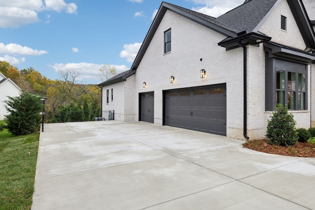 view of property exterior with brick siding, an attached garage, a shingled roof, and driveway