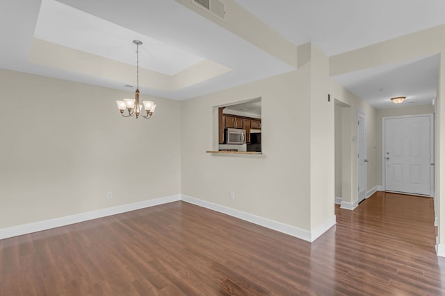 empty room with dark wood-type flooring, a raised ceiling, and an inviting chandelier