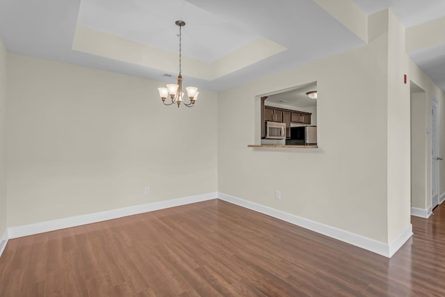 spare room featuring a notable chandelier, dark hardwood / wood-style floors, and a raised ceiling