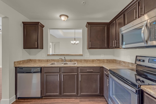 kitchen with sink, appliances with stainless steel finishes, hardwood / wood-style floors, hanging light fixtures, and a notable chandelier