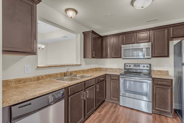 kitchen with stainless steel appliances, dark brown cabinets, sink, and dark hardwood / wood-style flooring