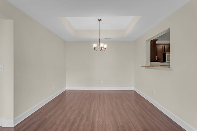 empty room featuring dark wood-type flooring, a tray ceiling, and a notable chandelier