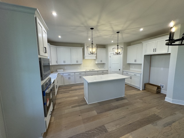 kitchen featuring hardwood / wood-style floors, a center island, decorative light fixtures, white cabinetry, and stainless steel appliances