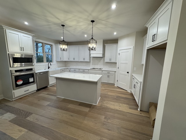 kitchen with appliances with stainless steel finishes, white cabinetry, a kitchen island, and hardwood / wood-style floors