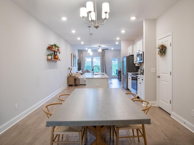 dining area with light hardwood / wood-style floors, ceiling fan with notable chandelier, and sink