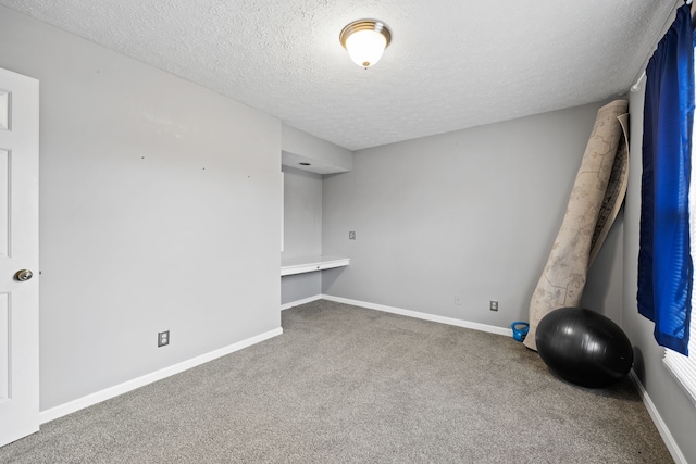 unfurnished room with carpet flooring, a textured ceiling, and built in desk