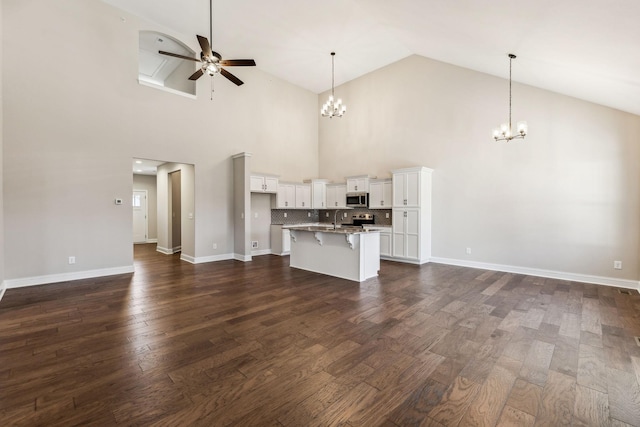 unfurnished living room featuring ceiling fan with notable chandelier, sink, dark wood-type flooring, and high vaulted ceiling