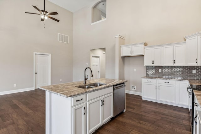 kitchen featuring white cabinets, sink, stainless steel dishwasher, a towering ceiling, and an island with sink