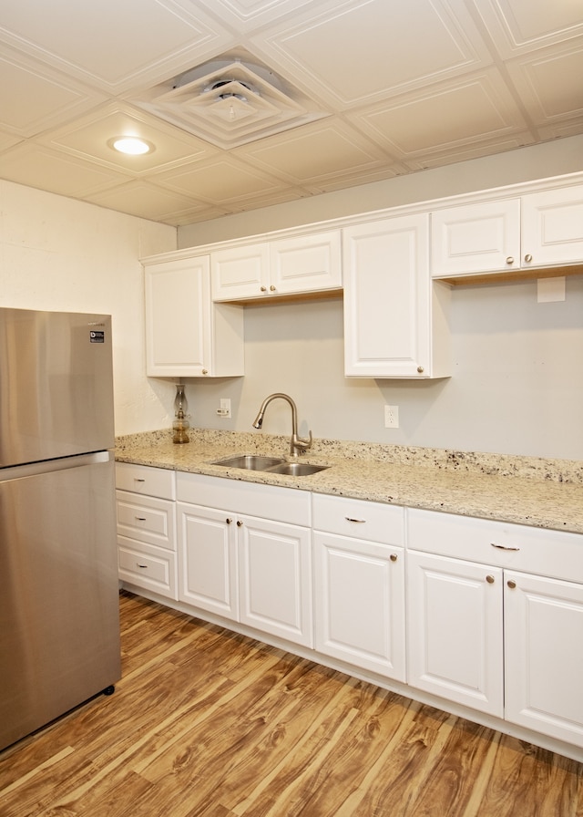 kitchen featuring white cabinets, sink, light wood-type flooring, light stone counters, and stainless steel refrigerator