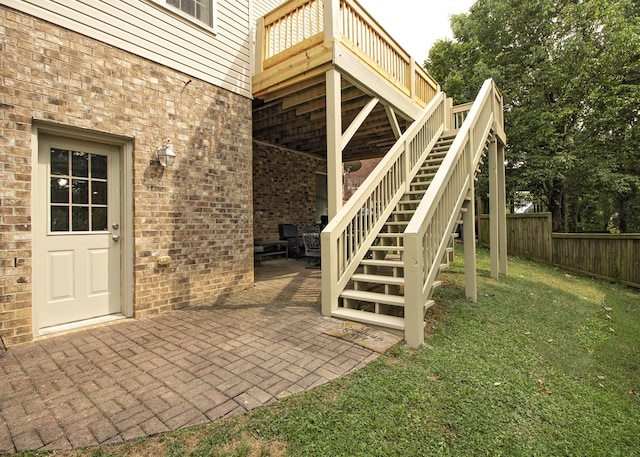 view of exterior entry featuring a lawn, a wooden deck, and a patio