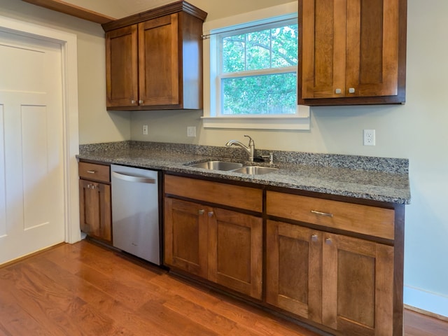 kitchen featuring stainless steel dishwasher, dark hardwood / wood-style floors, dark stone counters, and sink