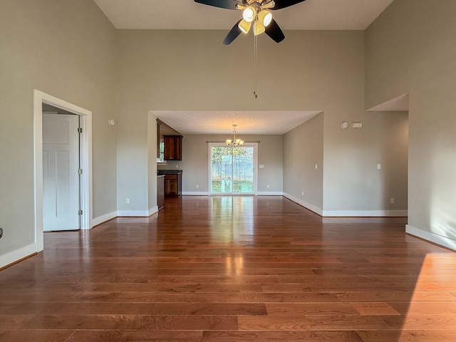 unfurnished living room featuring a high ceiling, ceiling fan with notable chandelier, and dark hardwood / wood-style flooring