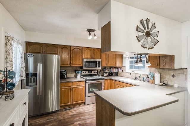 kitchen featuring sink, decorative backsplash, kitchen peninsula, appliances with stainless steel finishes, and dark hardwood / wood-style flooring