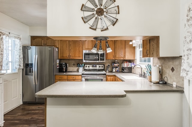 kitchen featuring stainless steel appliances, dark wood-type flooring, kitchen peninsula, sink, and tasteful backsplash