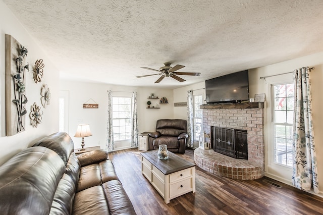 living room featuring a brick fireplace, dark hardwood / wood-style flooring, a textured ceiling, and ceiling fan