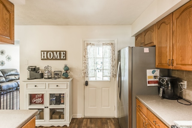 kitchen with dark wood-type flooring, stainless steel refrigerator, and decorative backsplash