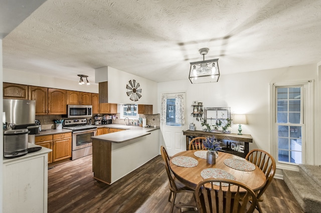 kitchen with kitchen peninsula, appliances with stainless steel finishes, dark wood-type flooring, and tasteful backsplash