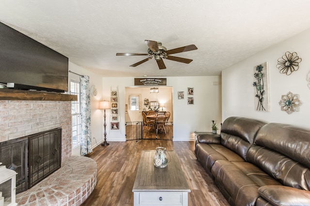 living room with ceiling fan, a textured ceiling, dark hardwood / wood-style floors, and a fireplace